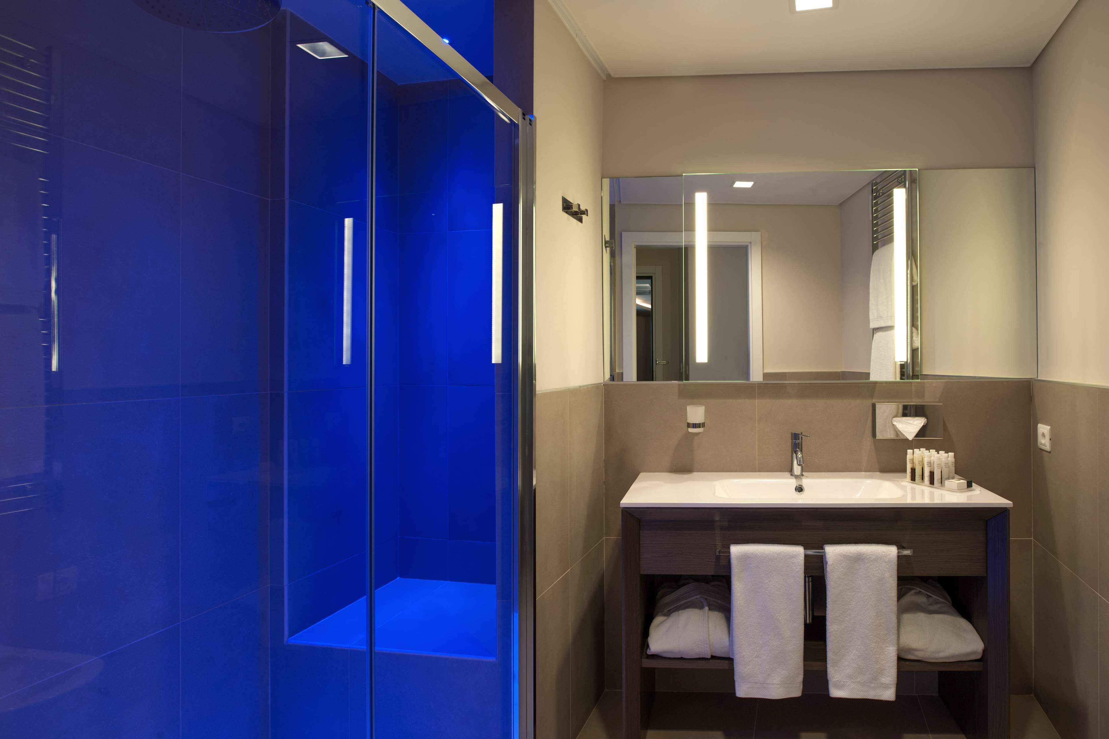A modern bathroom with a glass-enclosed shower, a sink with two towels, and a mirror above the sink.