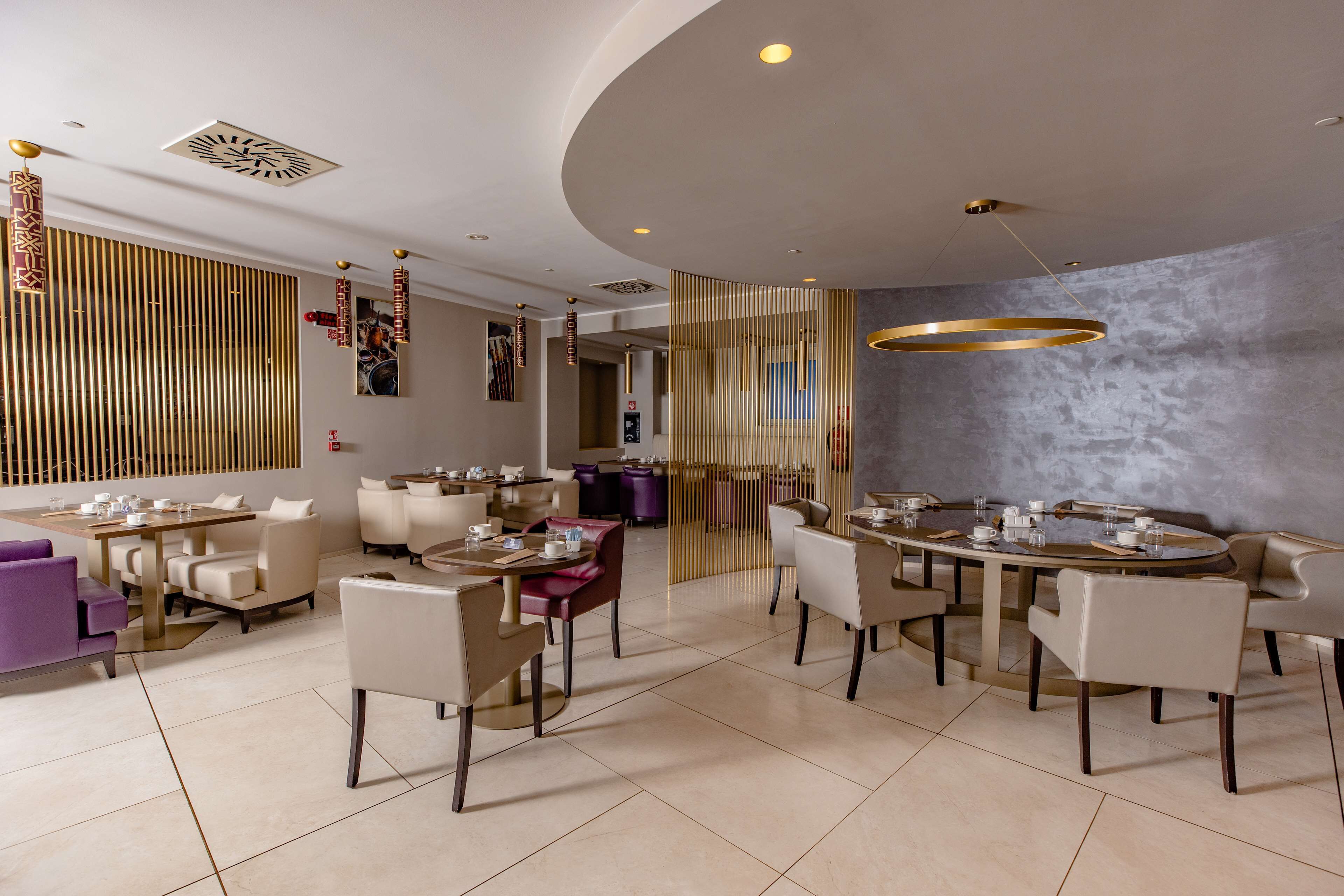 Un espace repas moderne avec des tables rondes, des chaises rembourrées et un plafond décoratif.