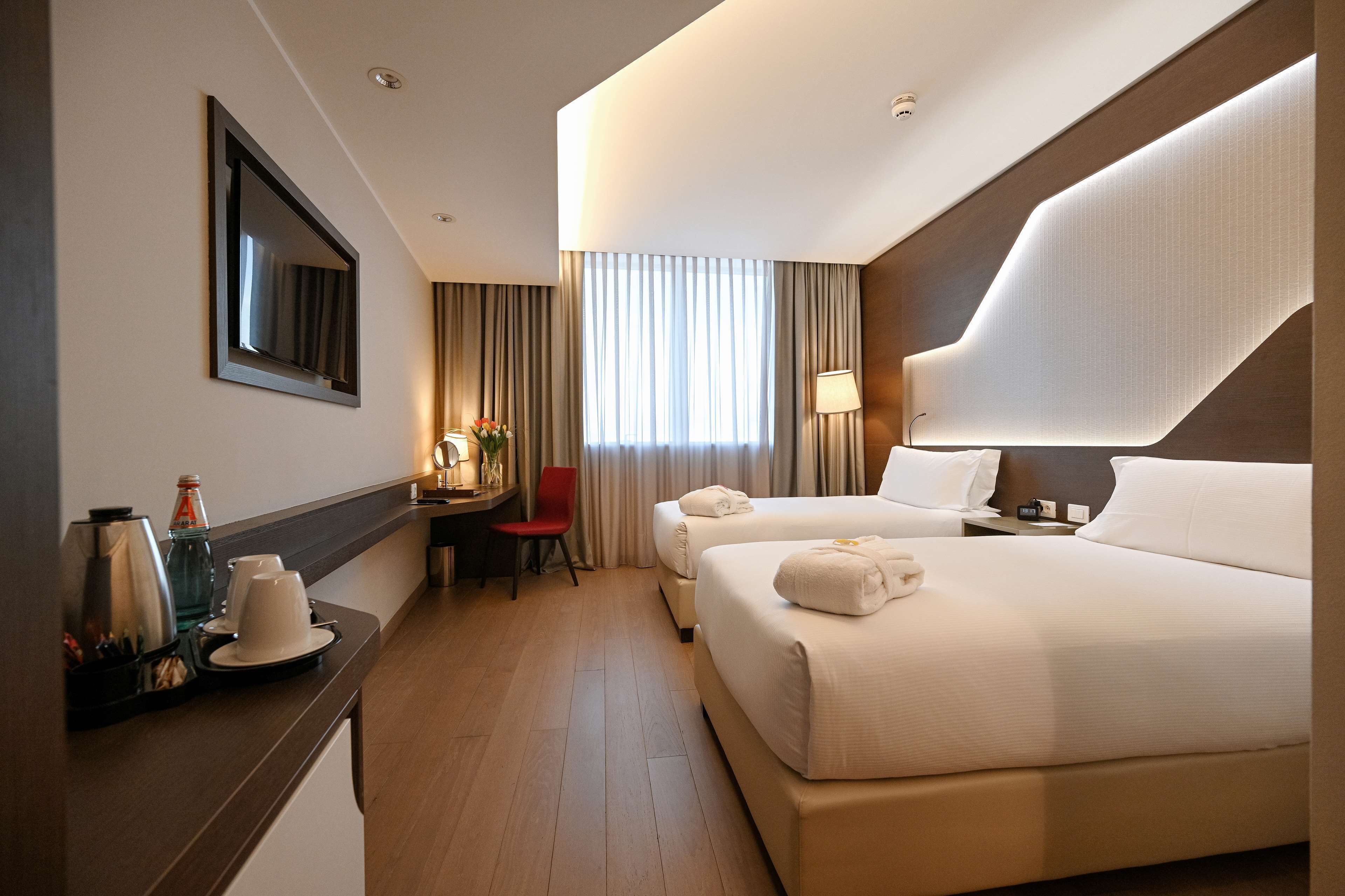 Een hotelkamer met twee bedden, een bureau met stoel, een koffiezetapparaat en een lamp.