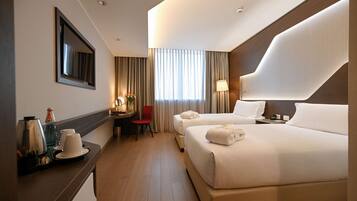 Een hotelkamer met twee bedden, een bureau met stoel, een koffiezetapparaat en een lamp.