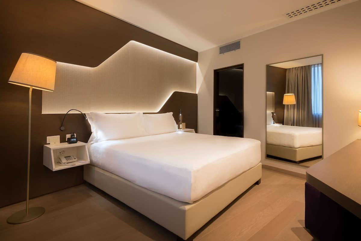 Ein modernes Hotelzimmer mit einem großen Bett, Nachttischen, einem Schreibtisch und einem Spiegel.