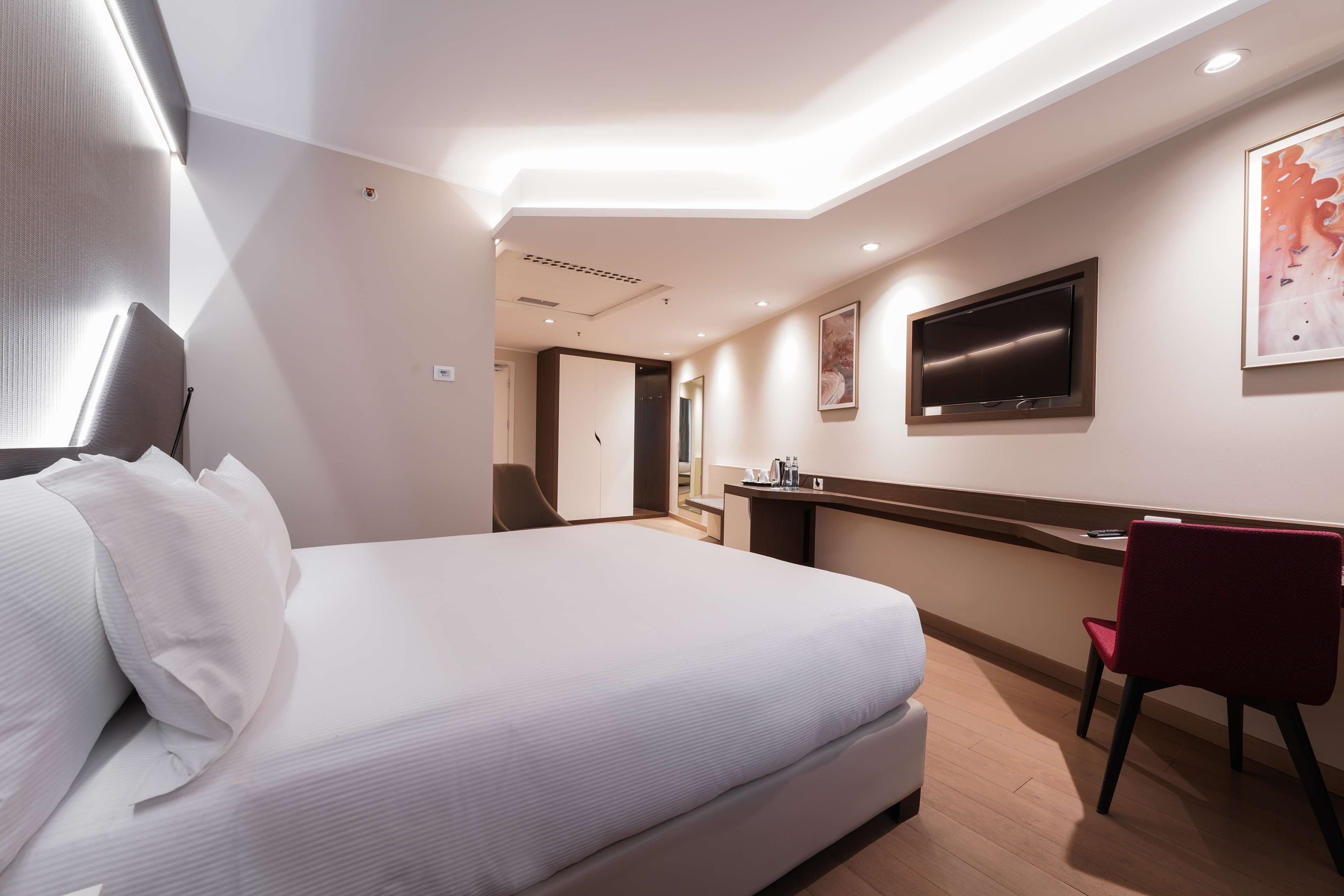 Une chambre d’hôtel moderne, dotée d’un grand lit, d’un bureau, d’une chaise, d’une télévision et d’œuvres d’art accrochées aux murs.