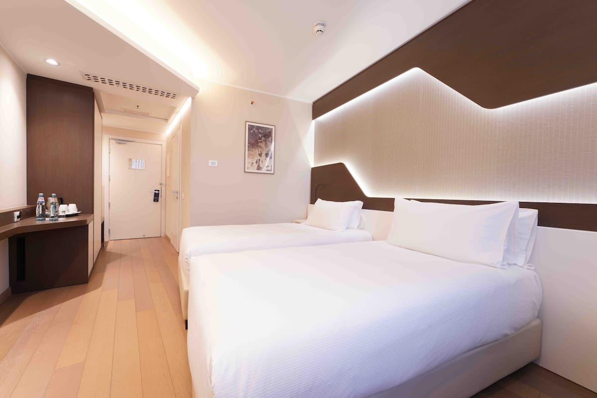 Ein Hotelzimmer mit zwei Betten, einem Schreibtisch und einer Badezimmertür.
