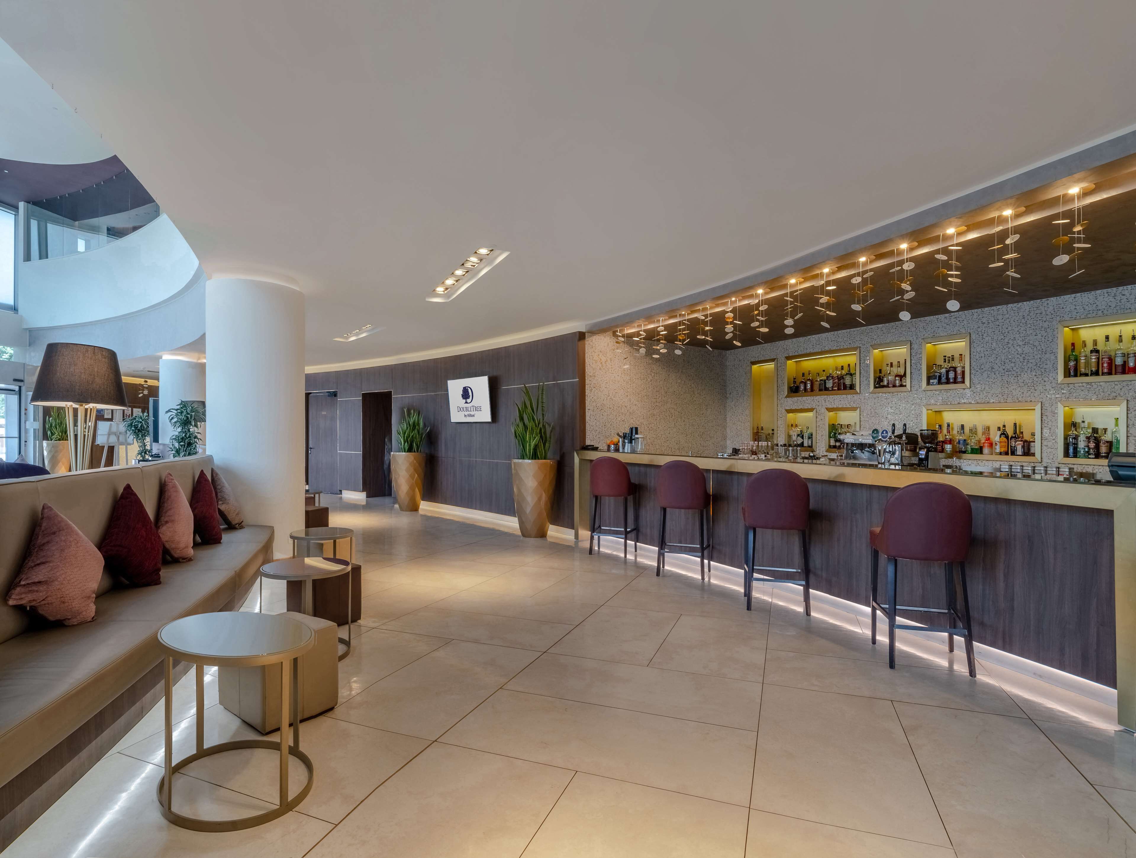A modern bar area with a curved counter, multiple stools, and a seating area with a sofa and round tables.