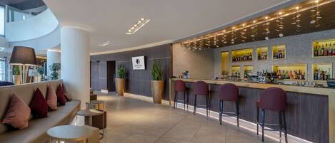 A modern bar area with a curved counter, multiple stools, and a seating area with a sofa and round tables.