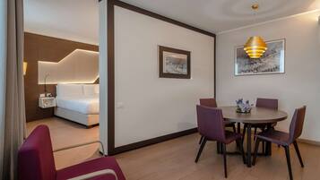 A modern hotel room with a bed, bedside table, and a dining area with chairs and a table.