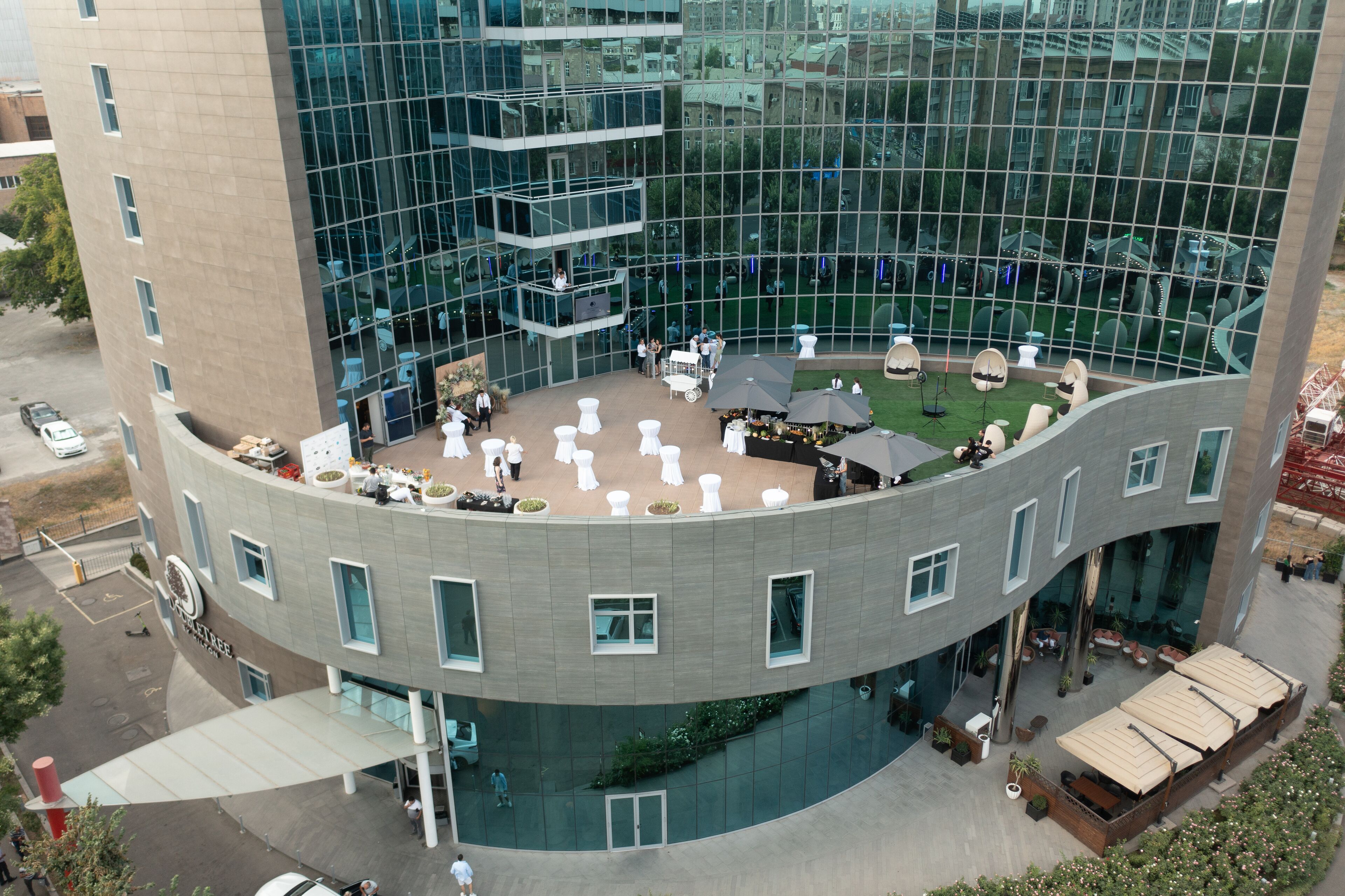 A modern hotel with a curved glass facade, outdoor seating area, and a central courtyard.