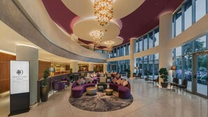 Un hall d’entrée spacieux avec un espace salon central, de grandes fenêtres et un lustre moderne.