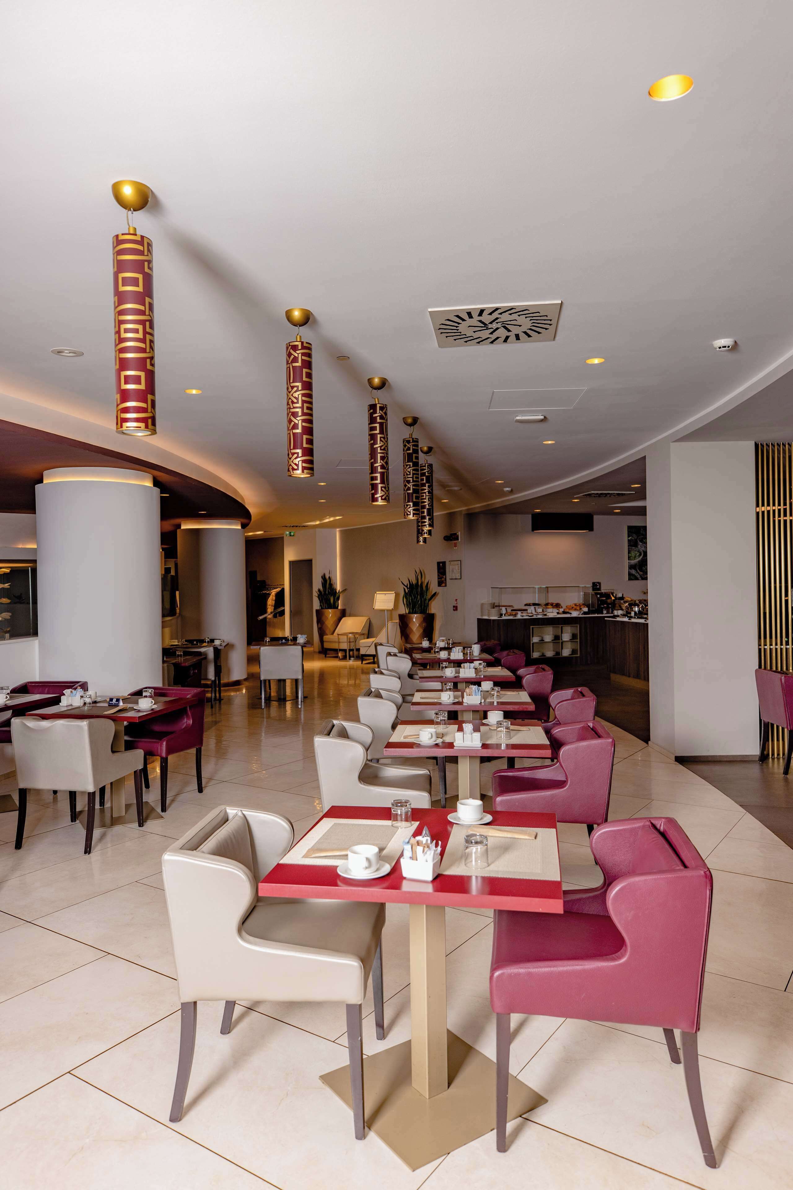 Ein modernes Restaurant mit langen Tischen, roten und weißen Stühlen und dekorativer Deckenbeleuchtung.