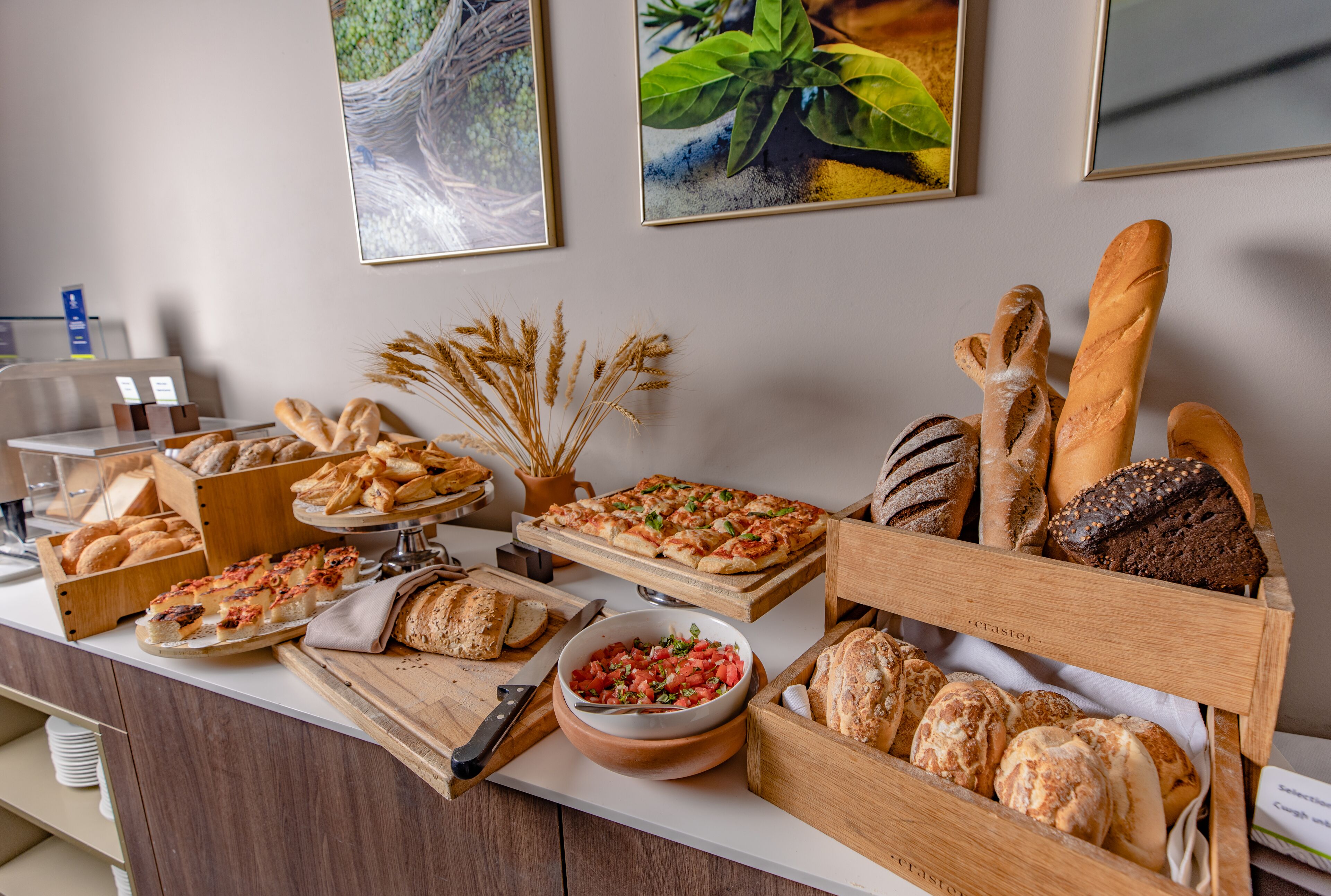 A buffet table with various breads, pastries, and a bowl of tomato salad.