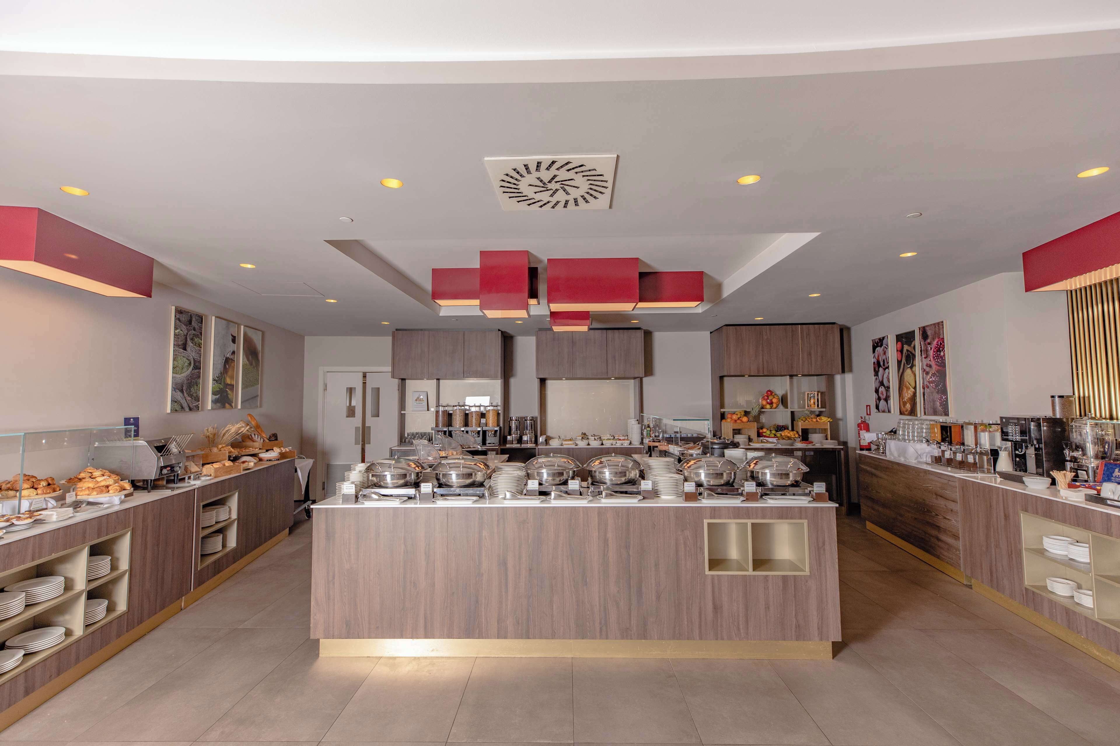Un moderno vestíbulo de hotel con una isla central que sirve comida, paneles de madera y luminarias contemporáneas.