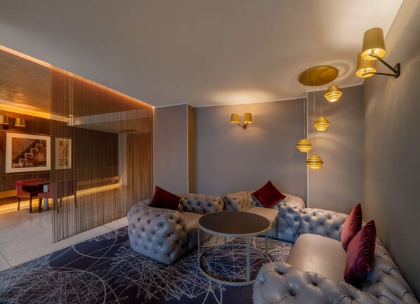 Un espace de détente moderne comprenant un canapé d’angle, une table basse ronde et des luminaires créant une ambiance chaleureuse.