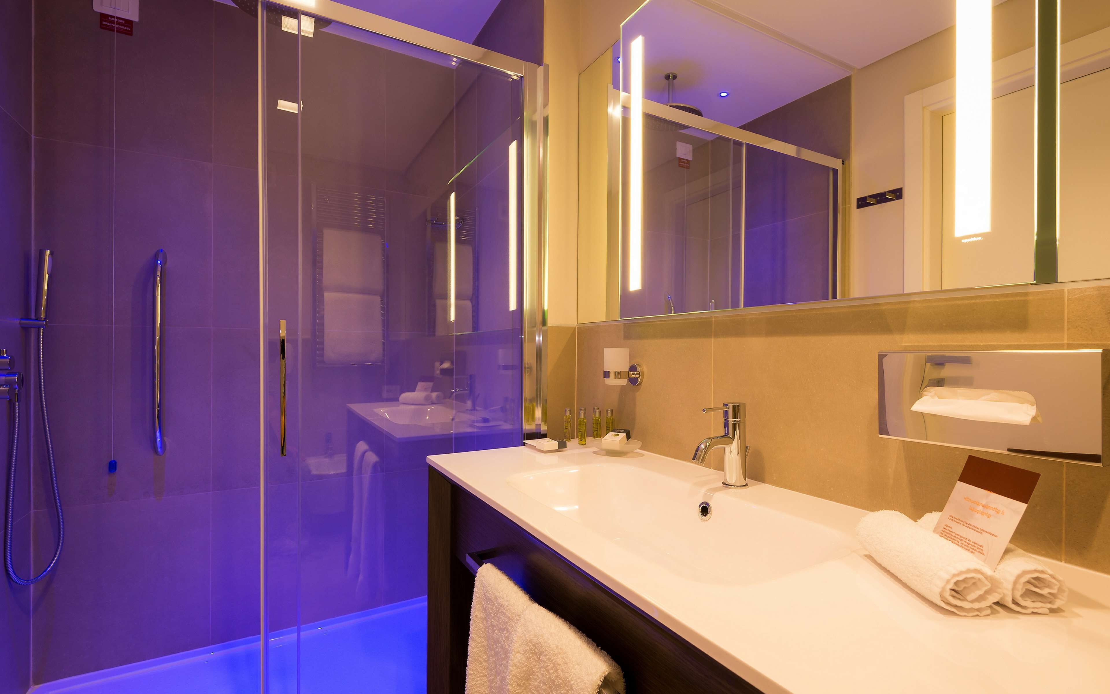 Un baño moderno con ducha de vidrio, lavamanos blanco y un espejo grande.