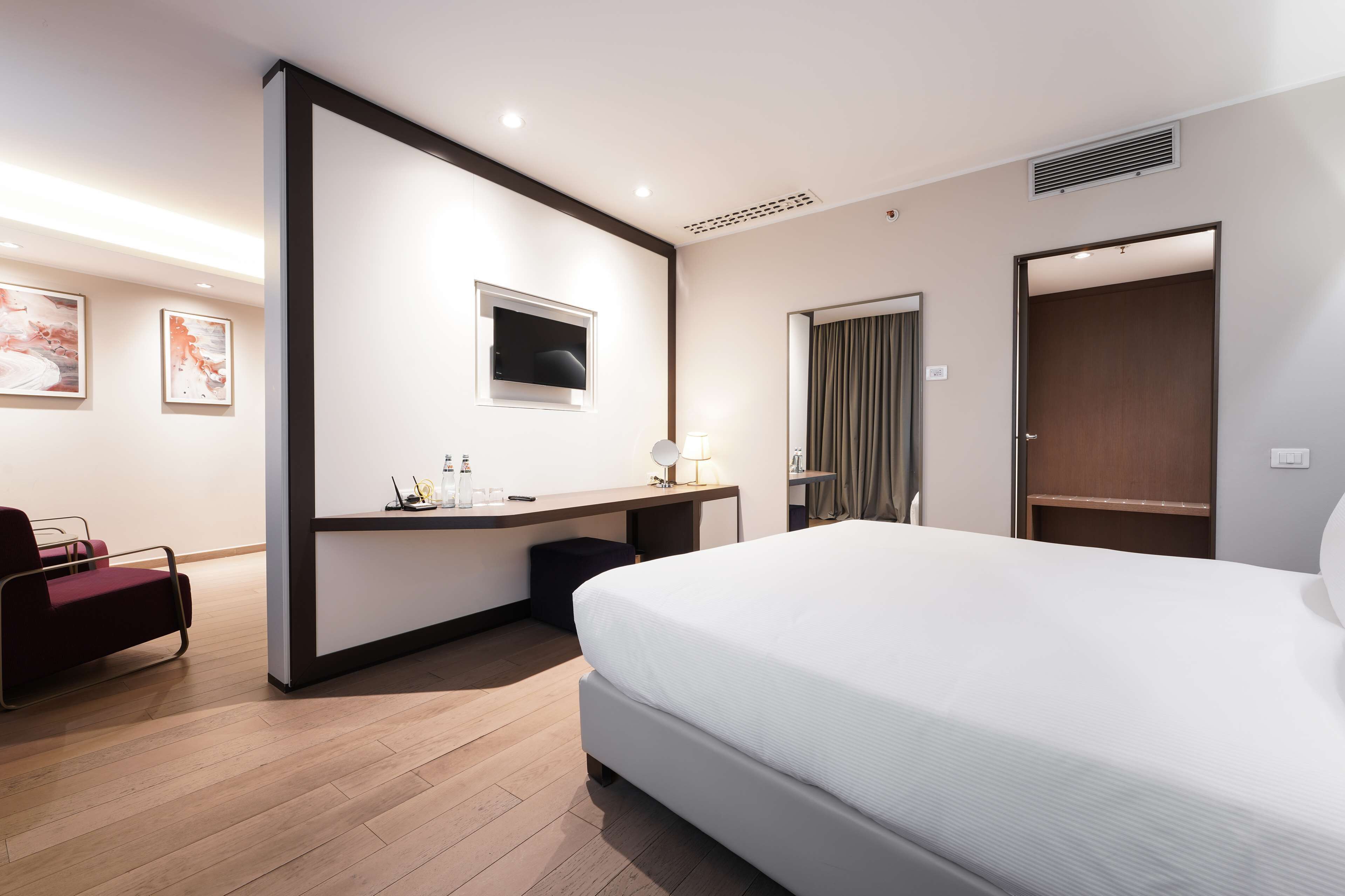 A modern hotel room with a large bed, a desk with a chair, a TV, and artwork on the walls.
