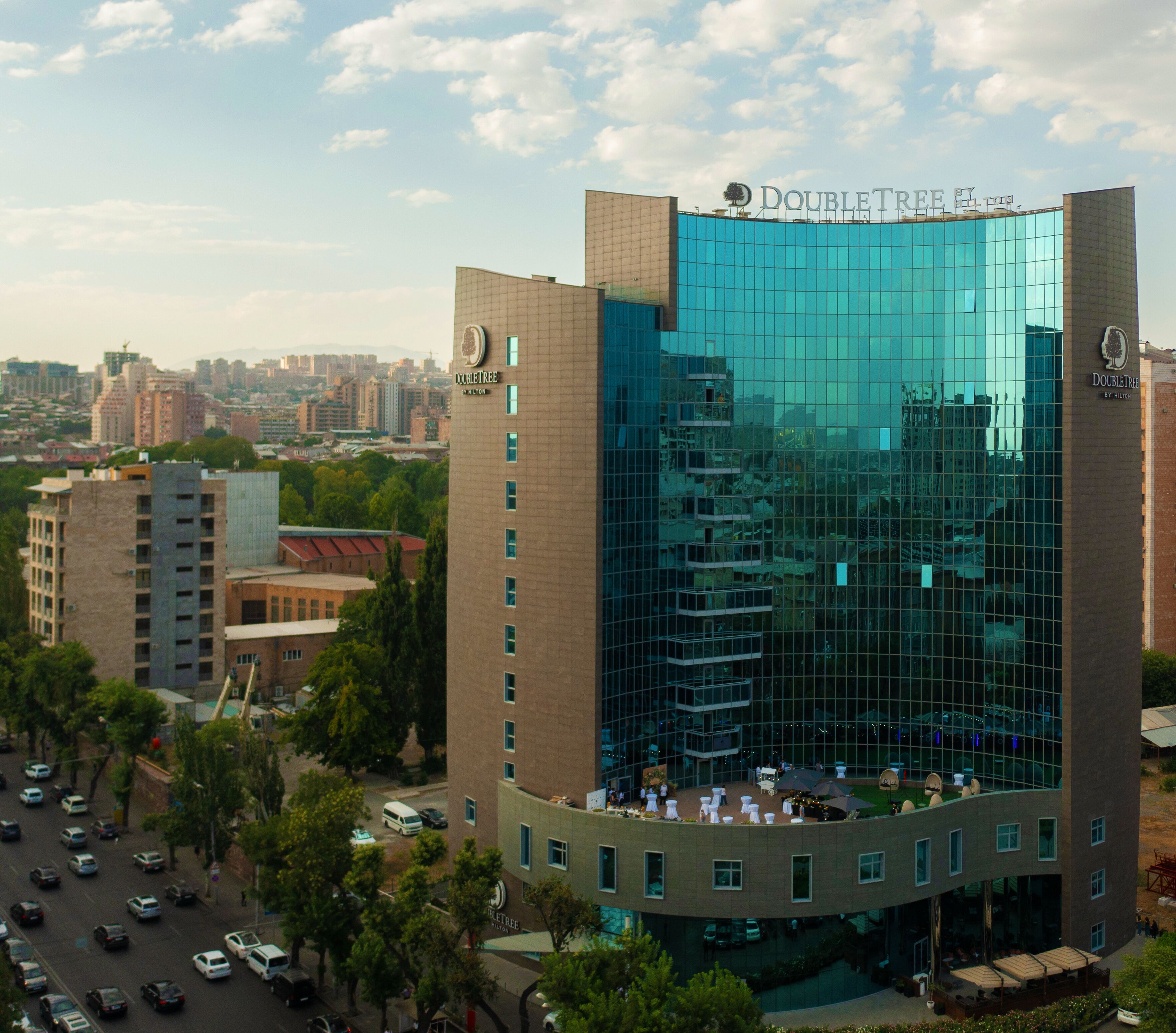 A DoubleTree hotel with a modern glass facade, surrounded by urban buildings and greenery.