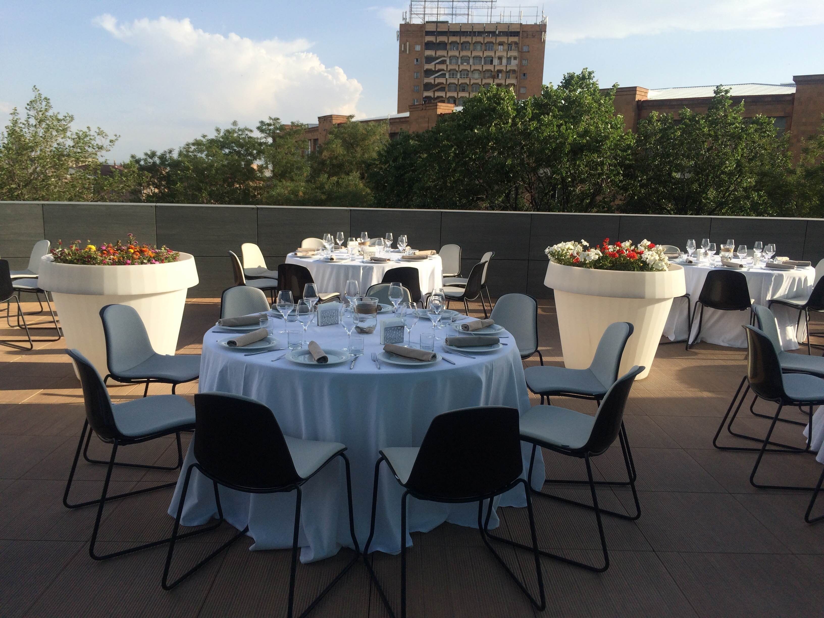 Un espace de restauration en plein air avec des tables rondes dressées pour un repas, entourées de chaises.
