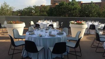 Un área de comedor al aire libre con mesas redondas dispuestas para una comida, rodeada de sillas.