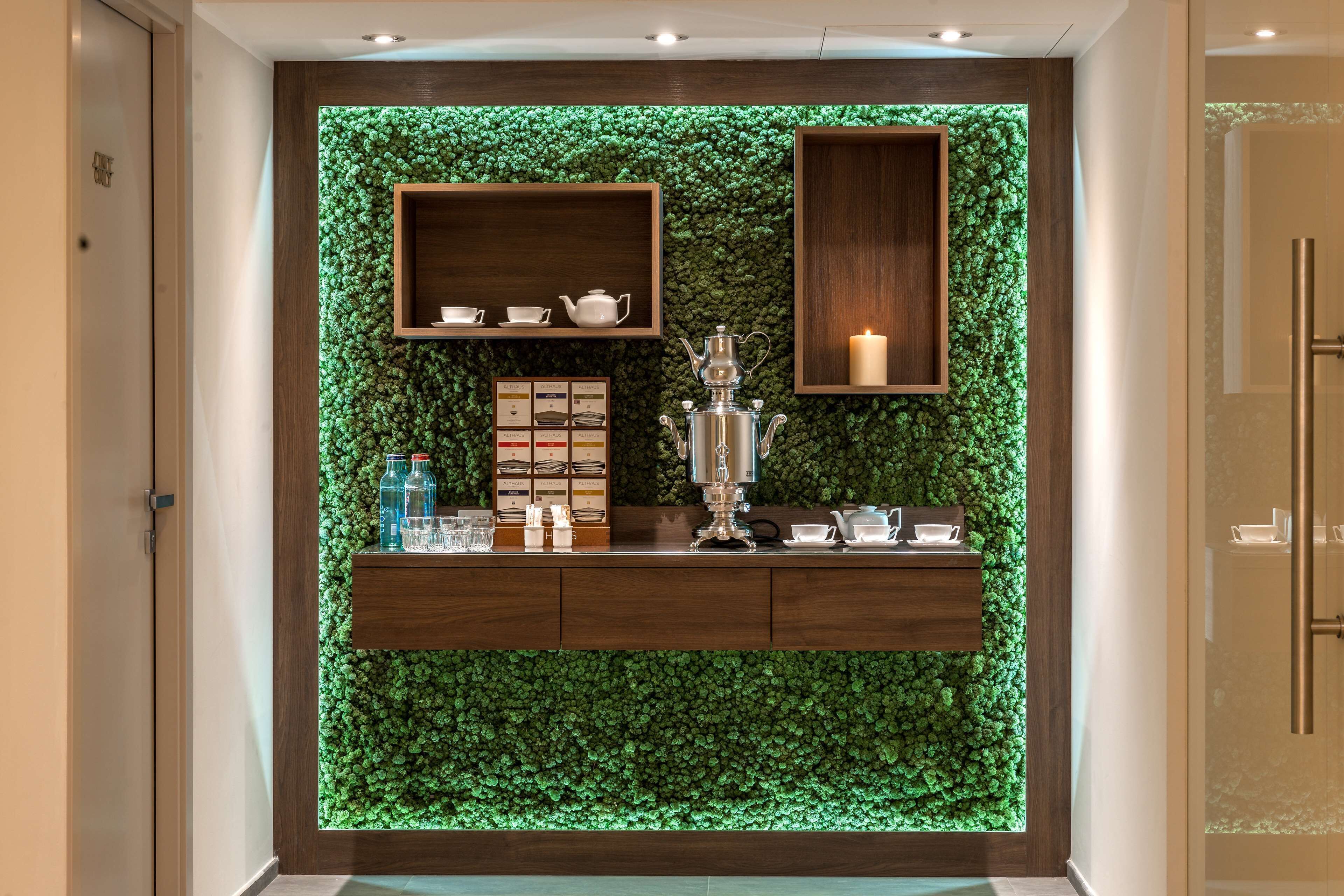 Un área de recepción con una pared verde, estantes de madera, un juego de té y una vela.