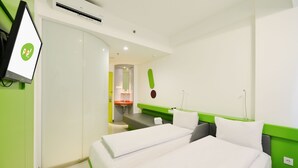 A hotel room with two beds, a green accent wall, a small kitchenette, and a TV mounted on the wall.