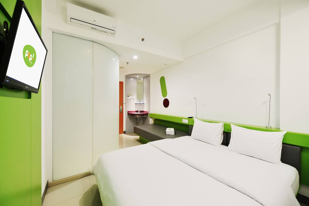 Habitación de hotel con cama, pared de acento verde, mesita de noche blanca, lavamanos rojo y espejo.