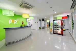 Uma área de recepção de hotel com uma parede verde, um balcão de recepção e uma máquina de vendas automática.