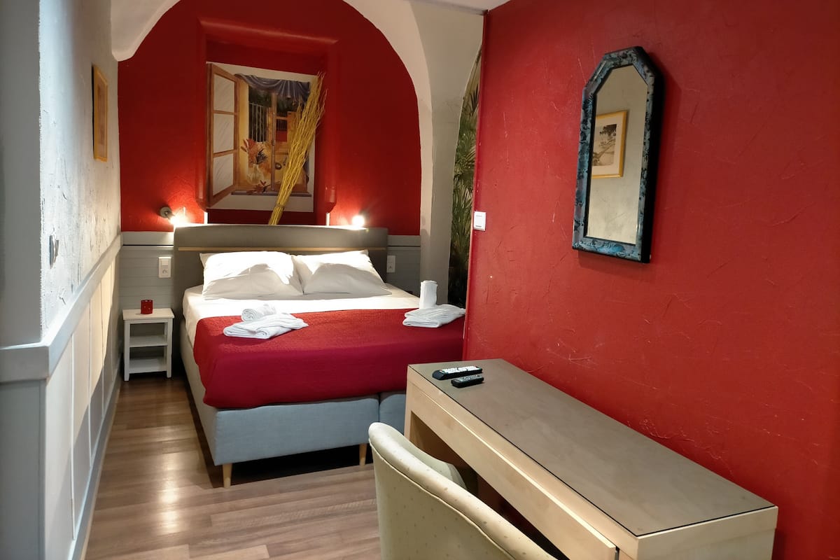 A hotel room with a bed, bedside tables, a desk, and a mirror.