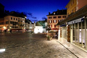 Une place pavée bordée de bâtiments historiques, avec une fontaine et un restaurant appelé « Auberge de Savoie ».