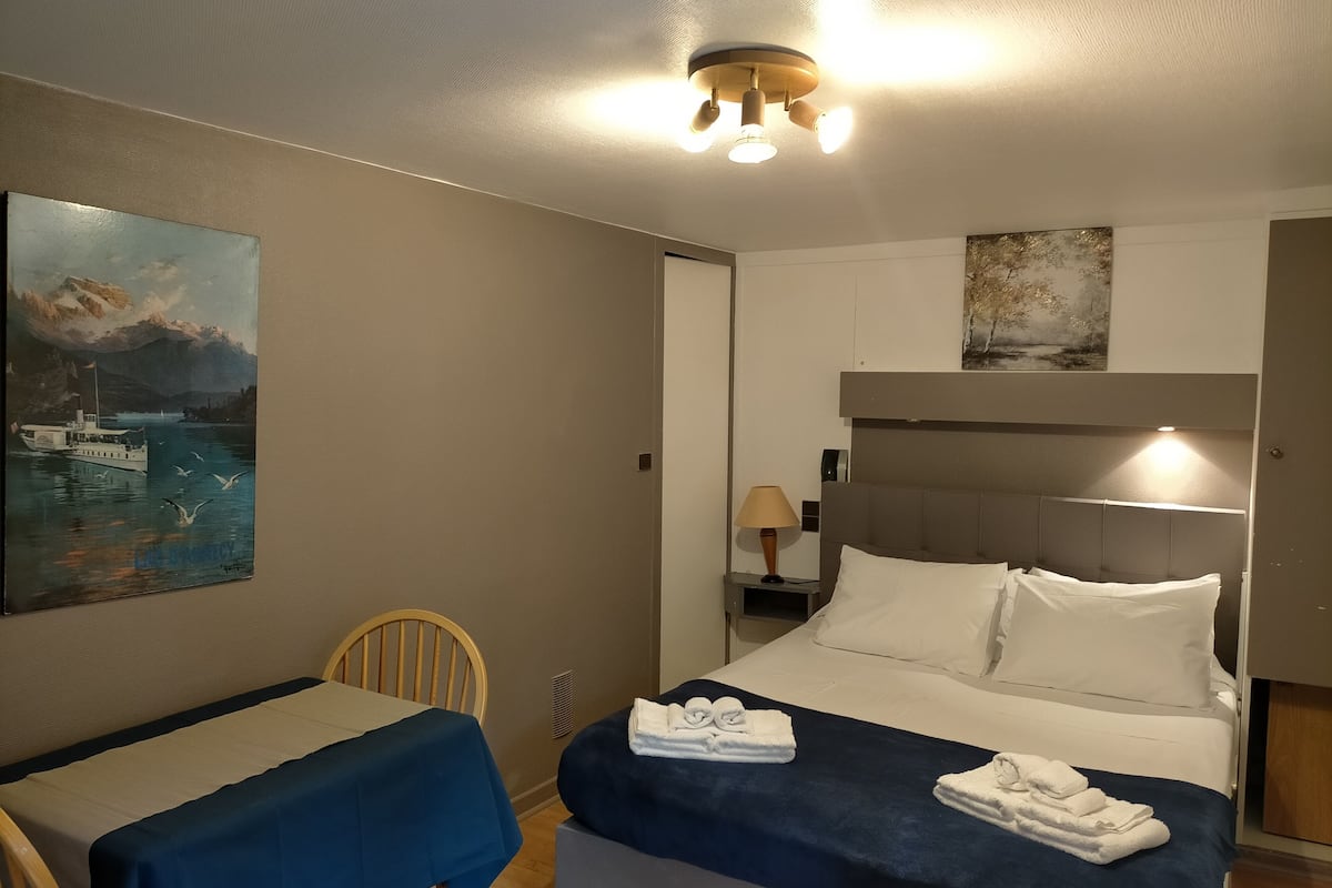 A hotel room with a bed, a table with a blue tablecloth, a chair, and artwork on the walls.