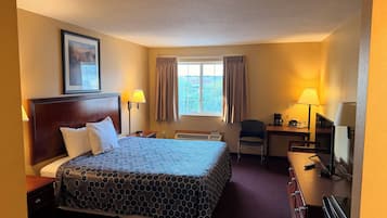 A hotel room with a large bed, a desk, a chair, a window with curtains, and a ceiling light.