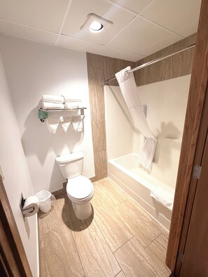 A bathroom with a toilet, a shower with a curtain, and a towel rack. - Pocahontas Inn & Suites (Pocahontas)