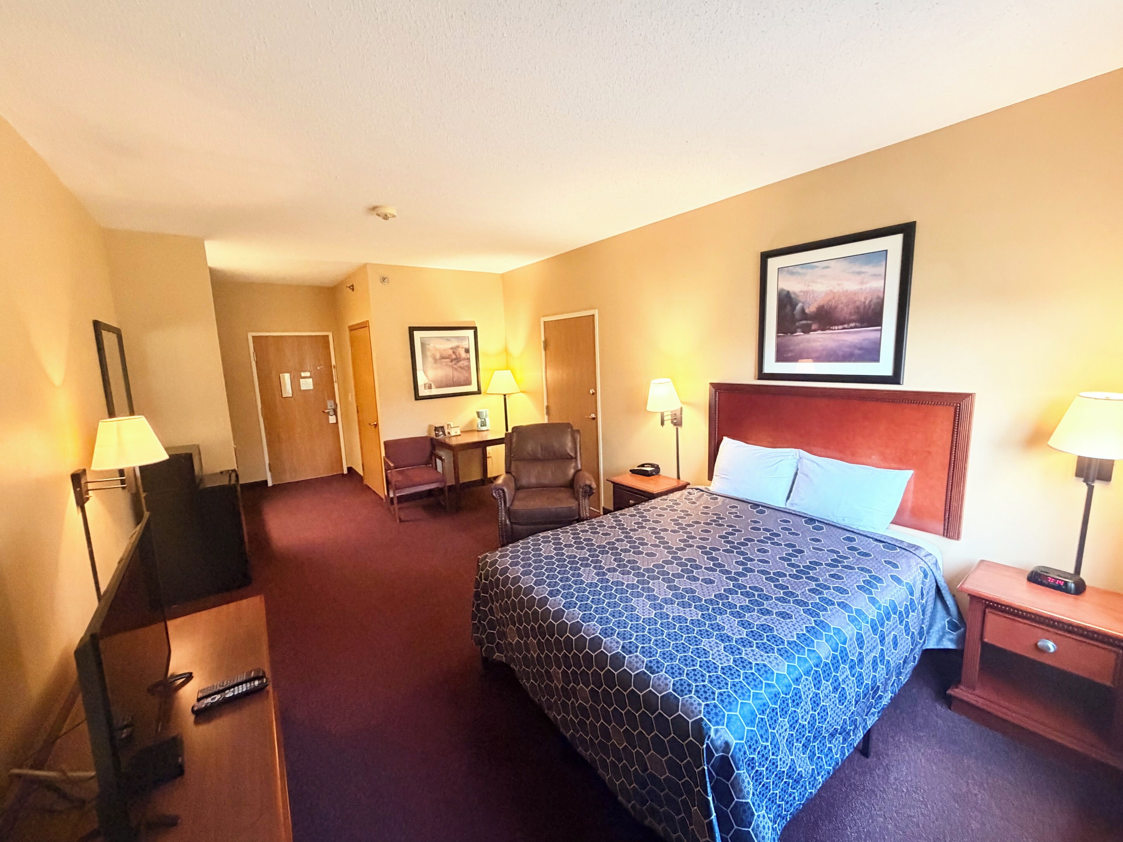 A hotel room with a bed, a desk, a chair, a TV, and a framed picture on the wall.