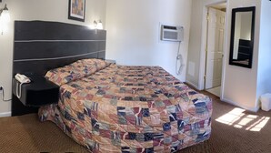 Un dormitorio con una cama grande, un escritorio con computadora, una silla, un teléfono y aire acondicionado instalado en la pared.
