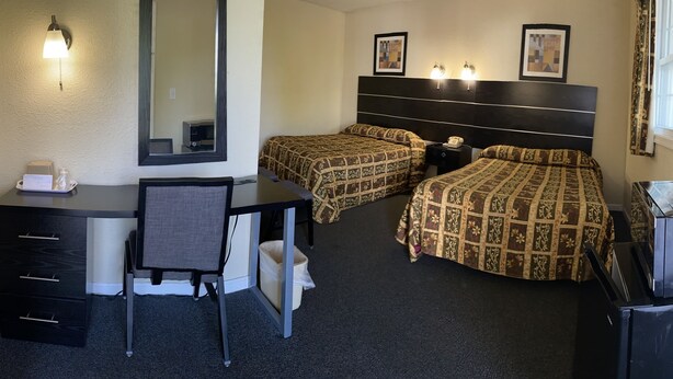 Habitación de hotel con dos camas, un escritorio, una silla, un aparador, un espejo y un televisor.