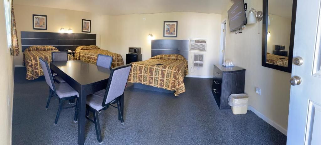 Habitación de hotel con dos camas, una mesa de comedor, sillas, un televisor y un espejo.