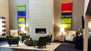 A lobby with green armchairs, a fireplace, and artwork on the walls. - Brookstone Lodge & Suites (Algona)