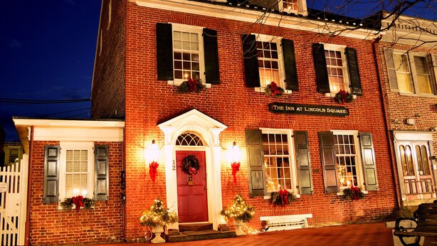 A brick building with a red door, multiple windows with shutters, and Christmas decorations. - Inn at Lincoln Square (Gettysburg)