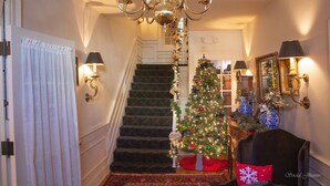 A staircase with a Christmas tree, a chandelier, and wall sconces. - Inn at Lincoln Square (Gettysburg)