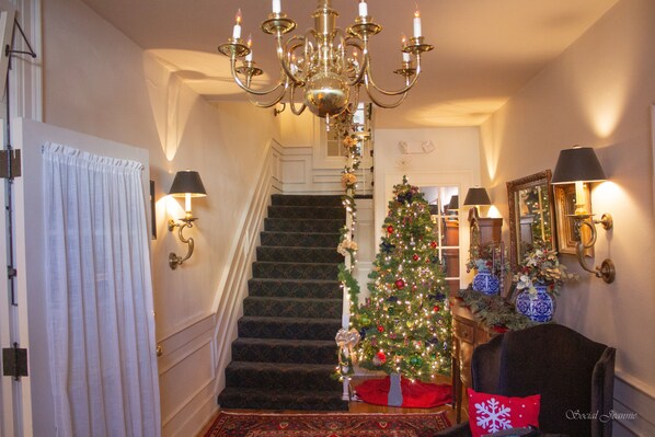 A staircase with a Christmas tree, a chandelier, and wall sconces.