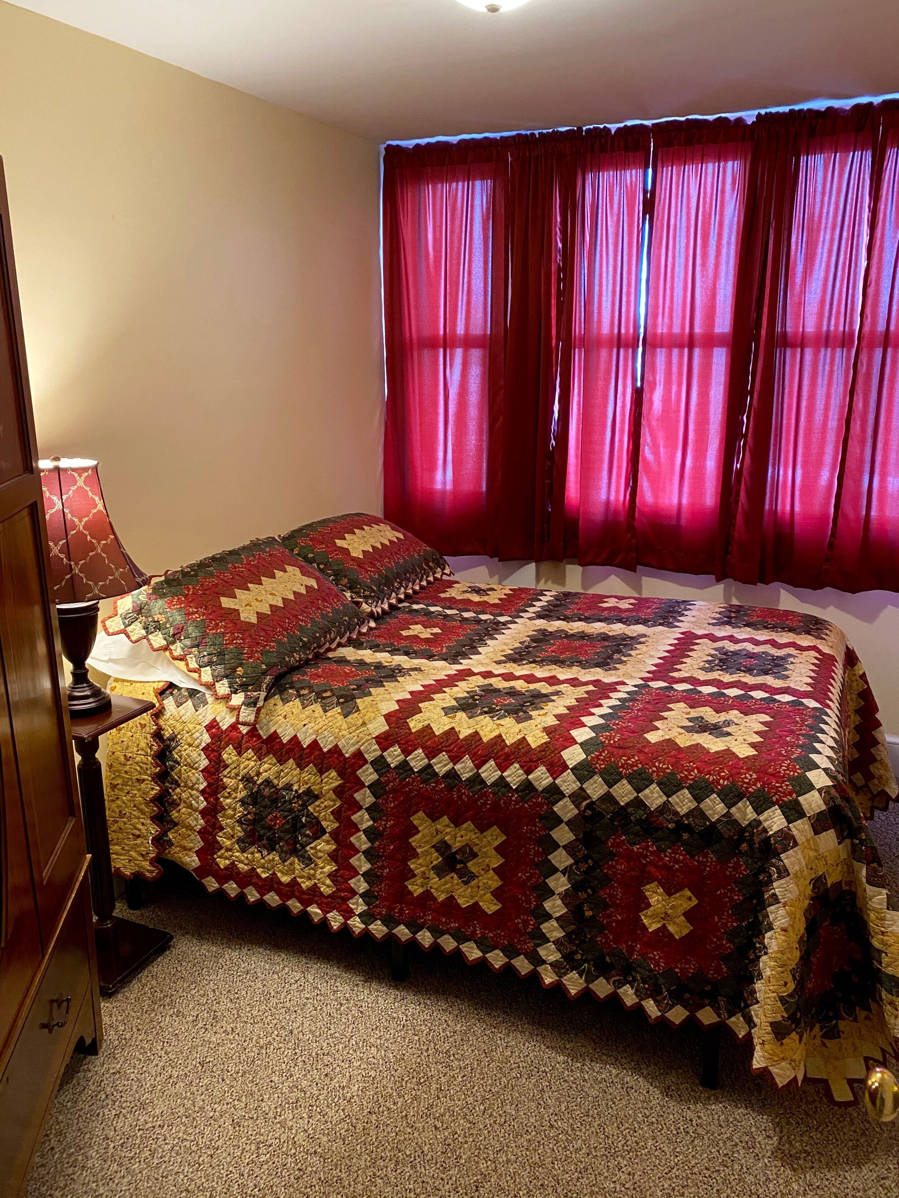 A bedroom with a large bed, red curtains, and a wooden nightstand.