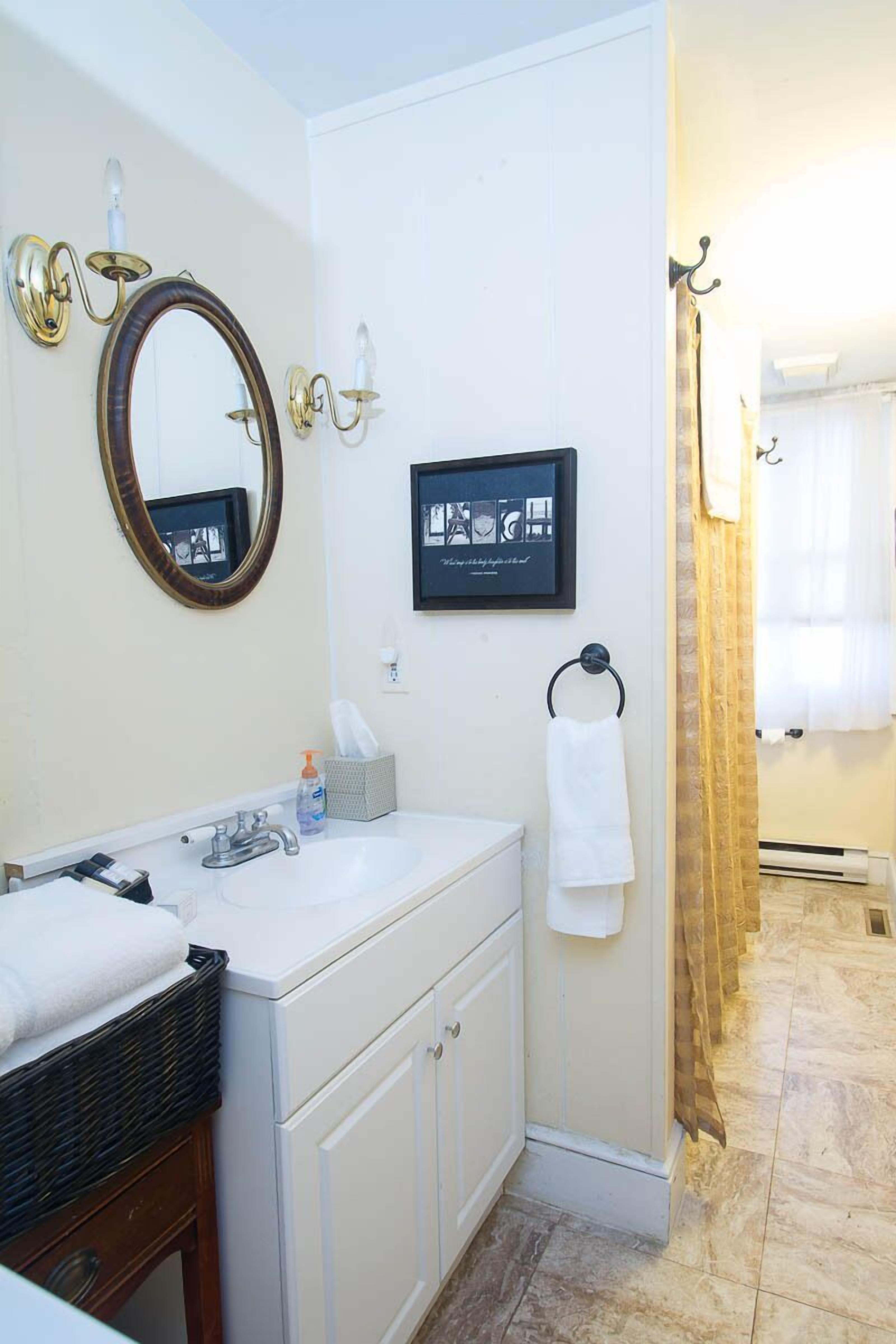 Un bagno con un lavandino bianco, uno specchio, un quadro incorniciato e un portascopevoli.