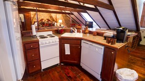 A compact kitchen with a stove, sink, and dishwasher, wooden cabinets, and a brick wall. - Inn at Lincoln Square (Gettysburg)