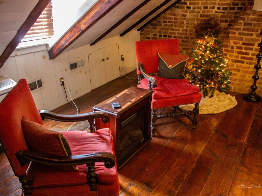 Una habitación acogedora con chimenea, dos sillones tapizados en rojo, una mesa de madera y un árbol de Navidad.