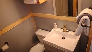 A bathroom with a white sink, a mirror, a toilet, and a wooden shelf with towels.