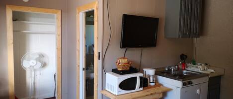 A compact kitchen with a microwave, sink, and a television mounted on the wall.