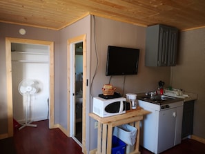 A compact kitchen with a microwave, sink, and a television mounted on the wall.