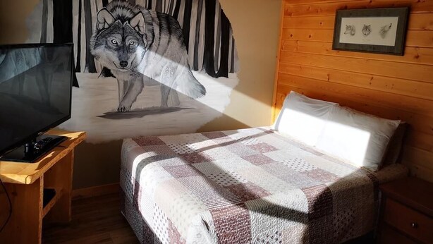 Una habitación acogedora con una cama, un televisor sobre un mueble de madera y un mural grande con un lobo.
