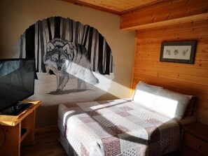 A cozy room with a bed, a television on a wooden stand, and a large wall mural of a wolf. - Overlook Inn & Cabins (Clearwater)