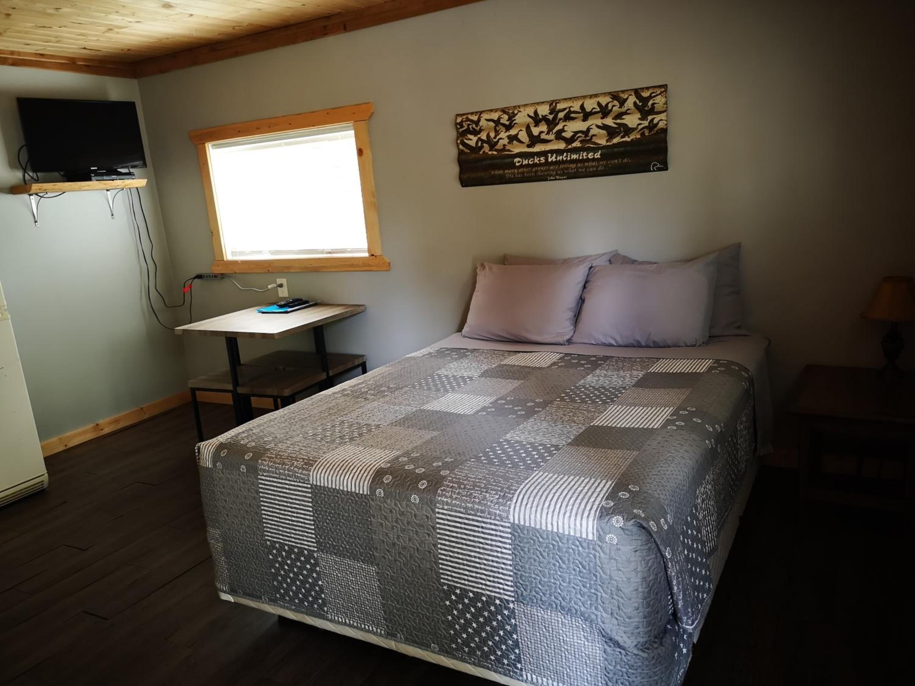 Un dormitorio con cama, escritorio, televisor y ventana.