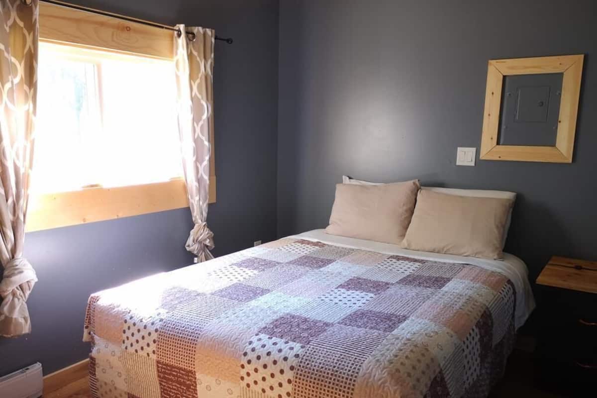 A bedroom with a large bed, a window with curtains, a wall-mounted picture frame, and a bedside table.