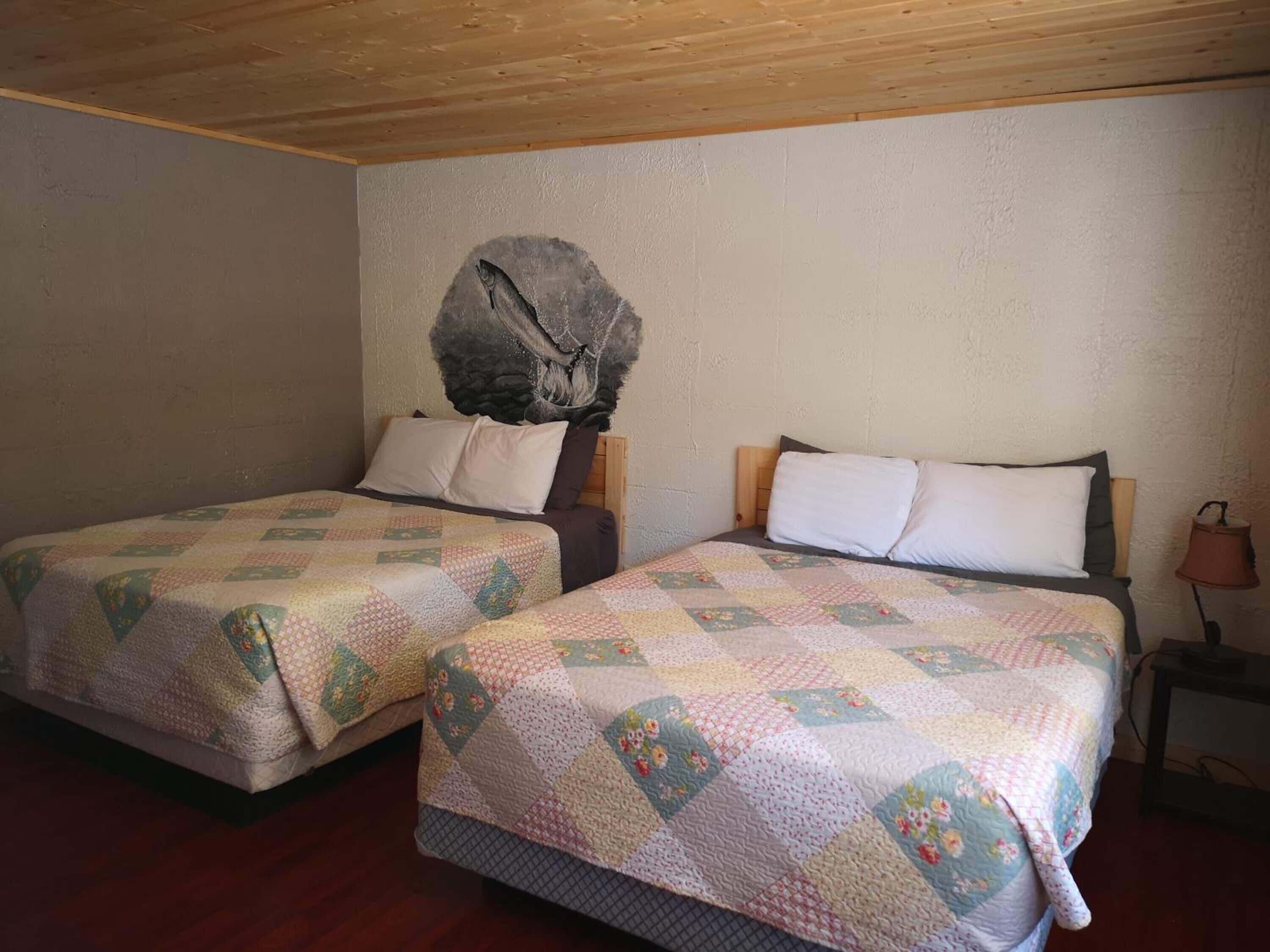 Een kamer met twee bedden, elk met een gewatteerde spreidek en kussens. Het linkerbed heeft een houten hoofdbord en het rechterbed een nachtkastje met een lamp.